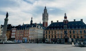 Vue de l’hôtel de ville de Lille sur la Grand-Place, avec son beffroi et les bâtiments historiques environnants, sous un ciel lumineux.