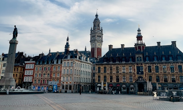Vue de l’hôtel de ville de Lille sur la Grand-Place, avec son beffroi et les bâtiments historiques environnants, sous un ciel lumineux.